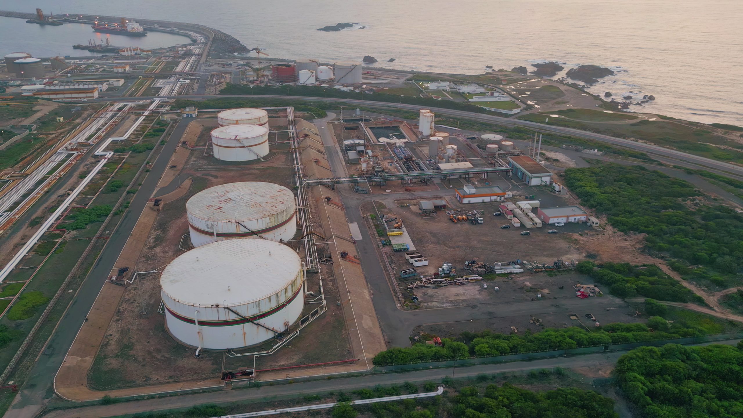 Imagem aérea de uma instalação de armazenamento e processamento de combustíveis fósseis próximo a uma área costeira