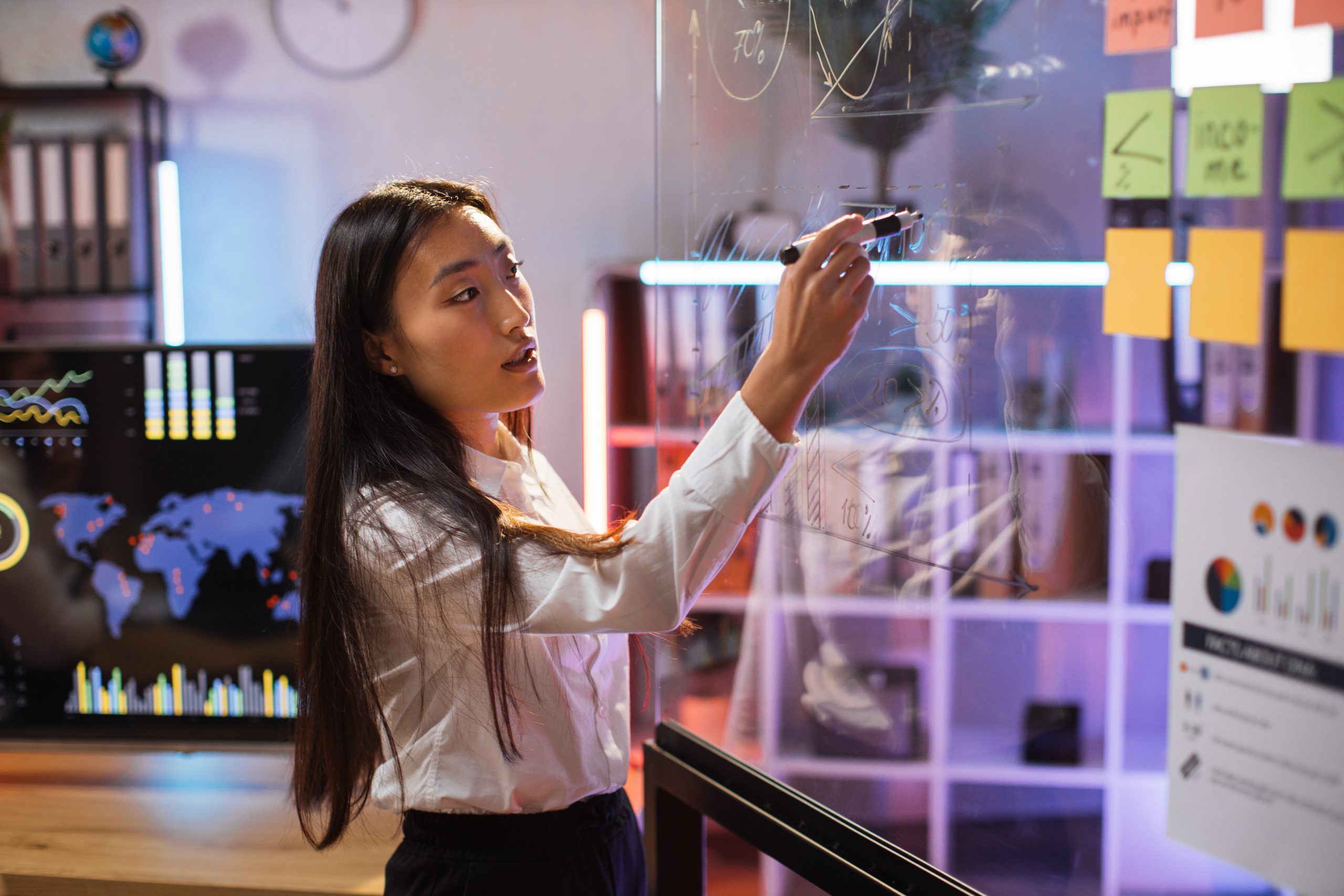 Mulher asiática líder vestindo traje formal escrevendo em um quadro transparente durante uma conferência na sala de escritório. Conceito de liderança feminina.