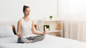 Mulher meditando, sentada sobre sua cama