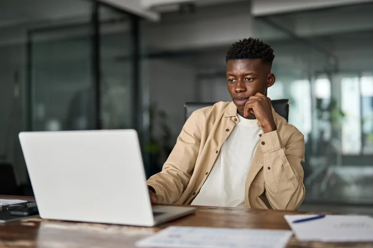 Homem negro olhando para a tela do seu laptop em um ambiente de trabalho. Conceito: Estruturando prompts para ChatGPT