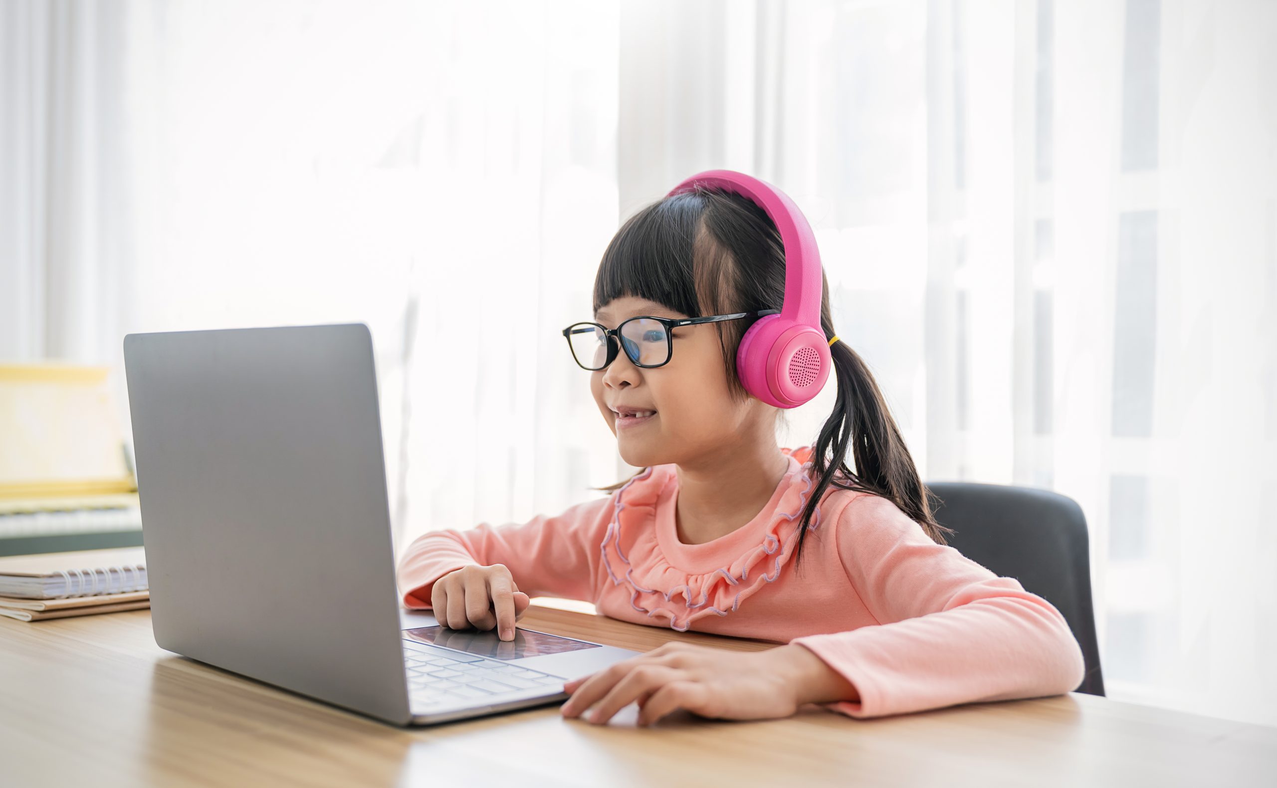 Uma criança asiática sorridente assiste a uma aula online em seu notebook. Conceito: tecnologia na educação