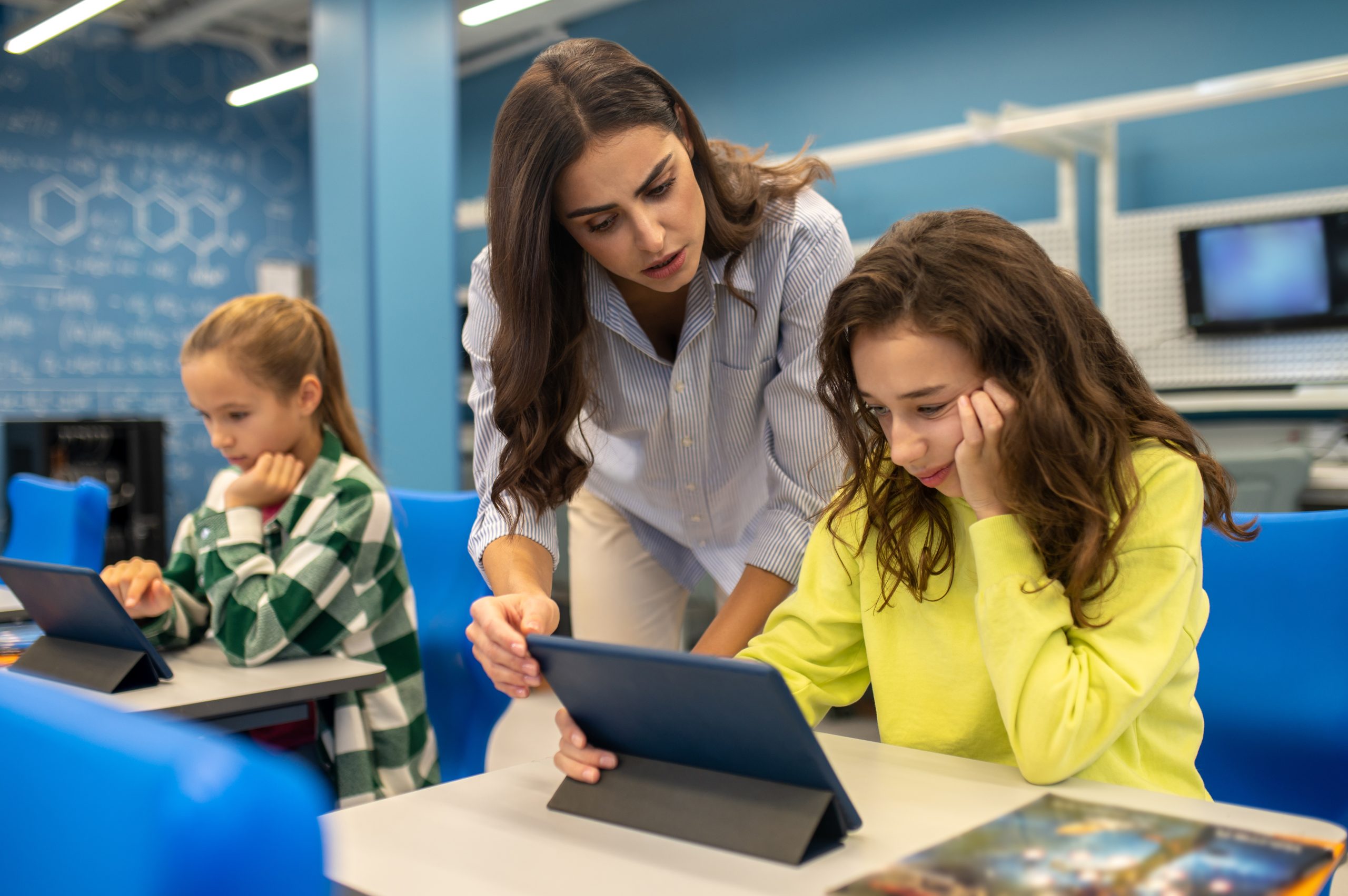 Uma professora conversando com uma estudante diante de um tablet em uma sala de aula