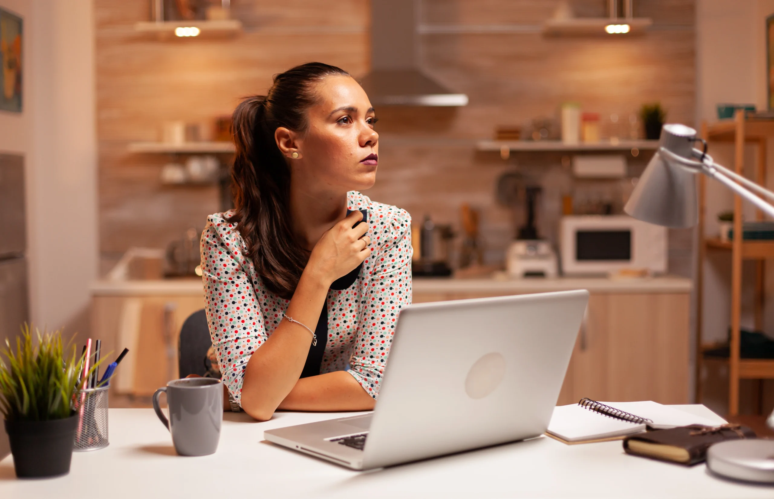 Mulher sentada à mesa com seu laptop aberto e pensando como montar um plano de carreira