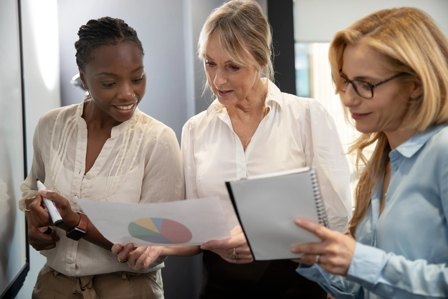 Três mulheres executivas em pé olhando para gráficos, representando equidade de gênero