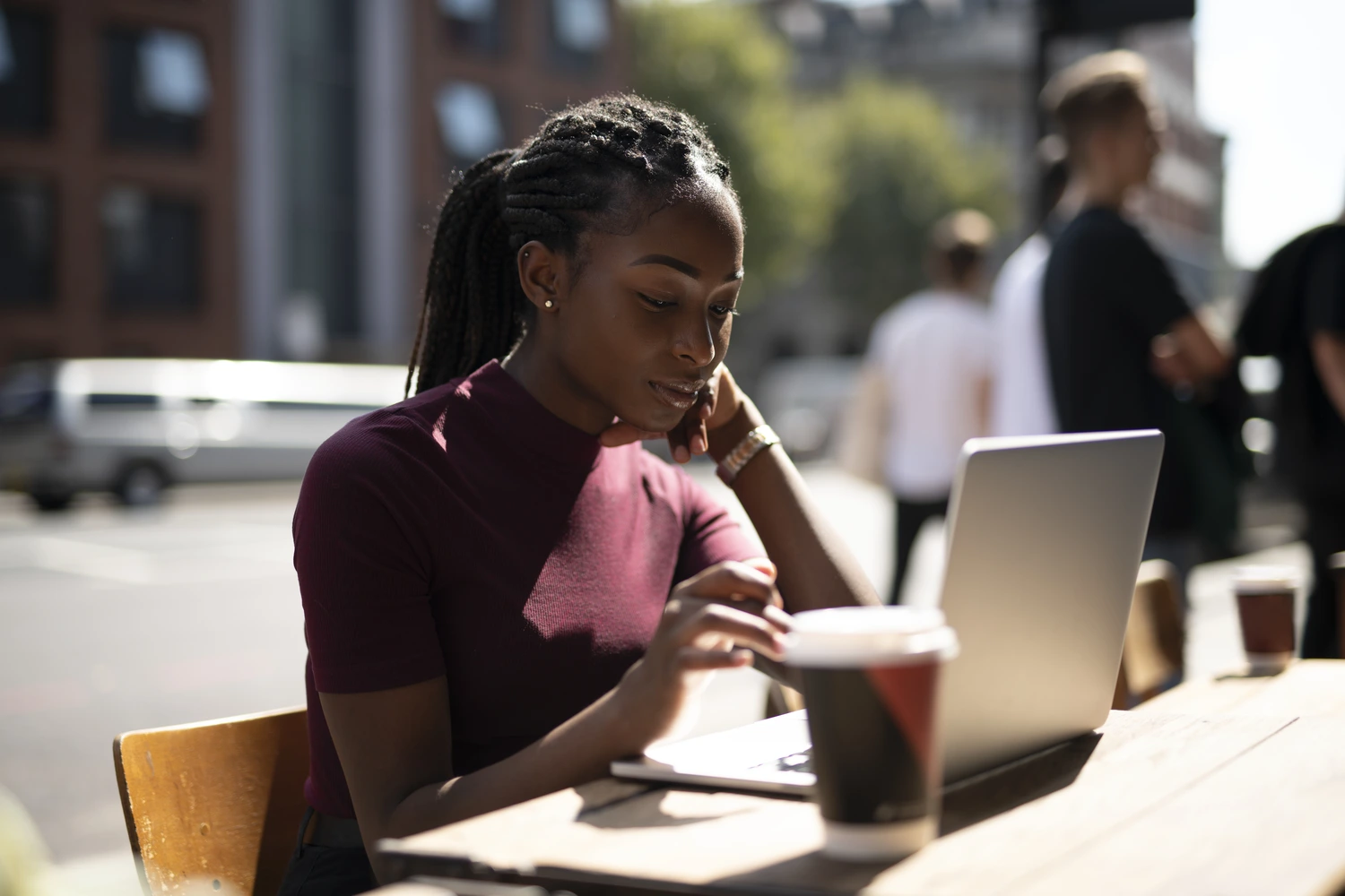 Uma mulher negra trabalhando em seu laptop de um café com sua mesa a céu aberto. Conceito: o que é trabalho remoto.