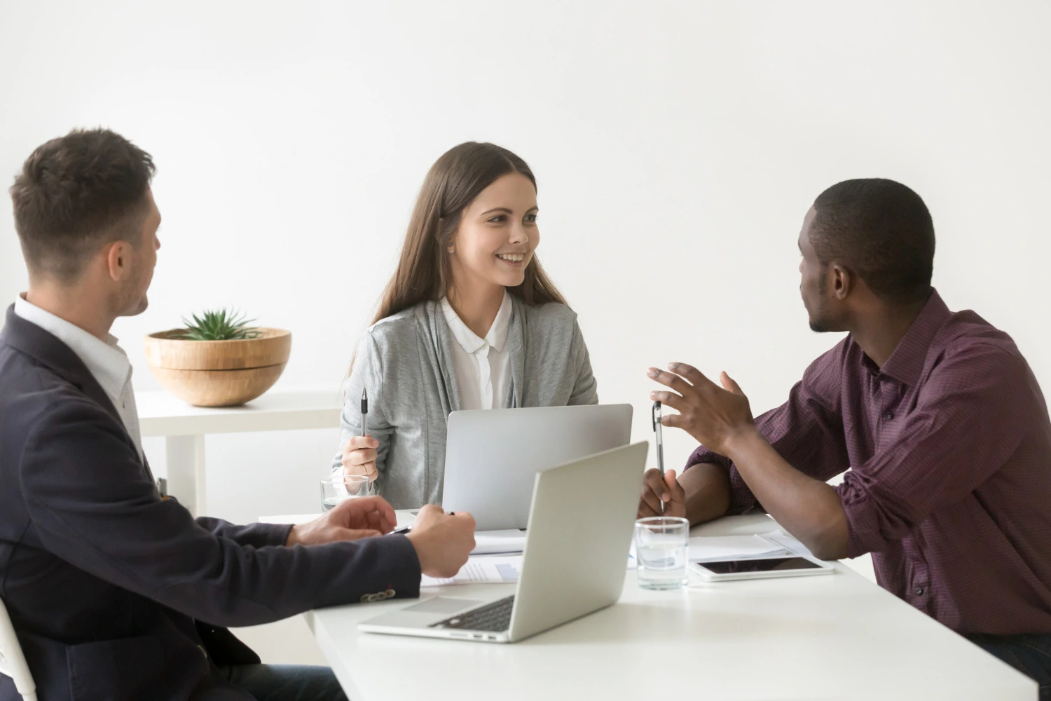 Três pessoas em reunião de feedback construtivo, conversando sorridentes e pensando em melhorias.