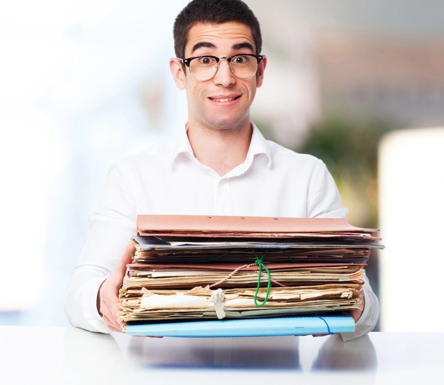 Homem segurando uma grande pilha de pastas e documentos, representando a um aspecto de trabalho de um assistente administrativo.