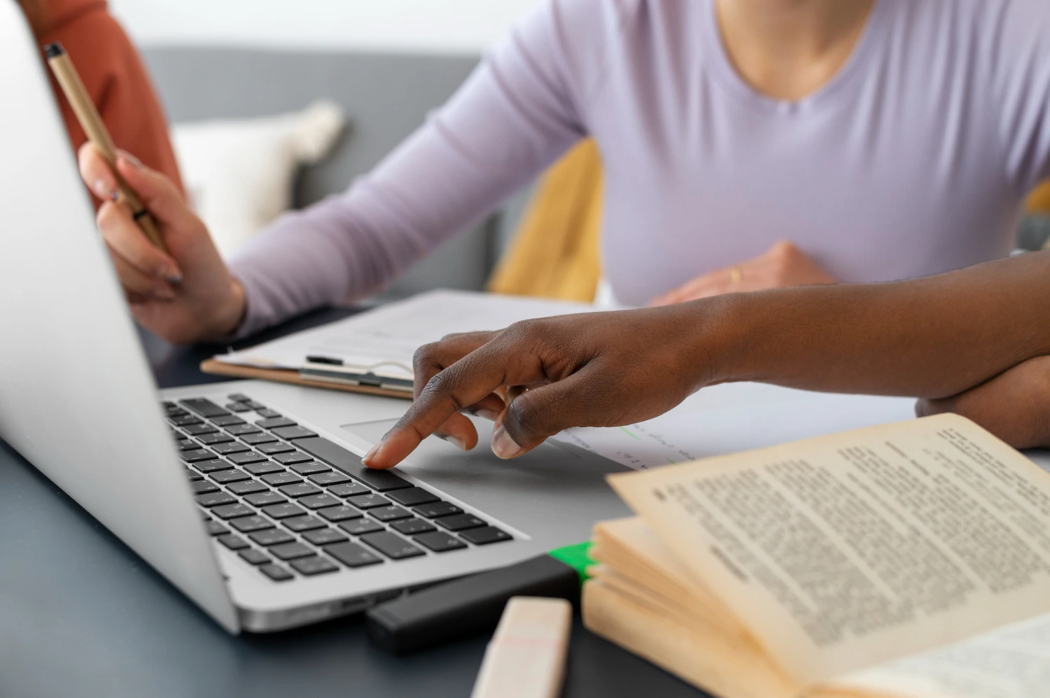 Mãos de estudantes interagindo com um laptop e materiais de estudo, representando o aprendizado colaborativo na Fênix Educação.
