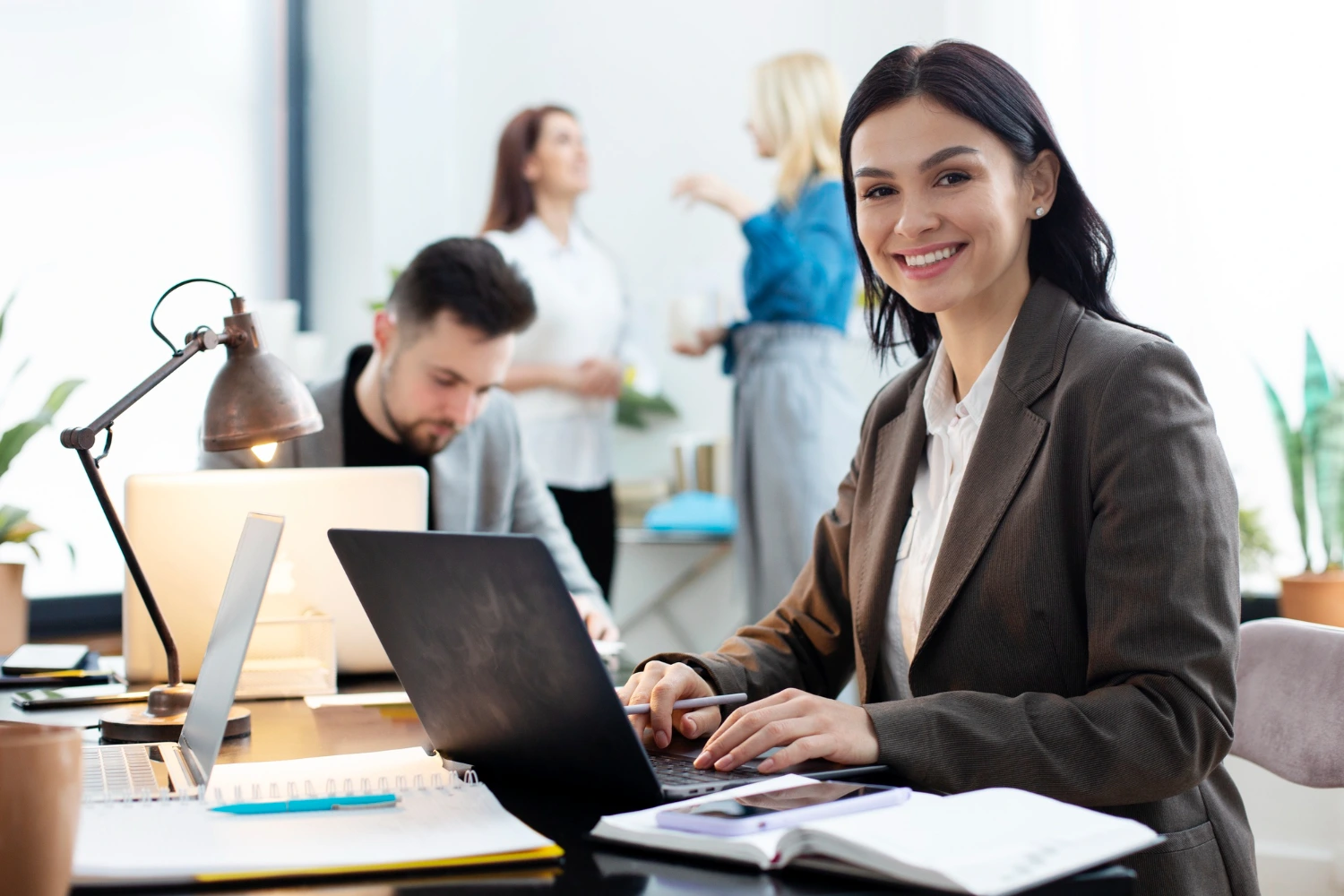 Uma gerente administrativa digitando no computador, no escritório de sua empresa, com sua equipe