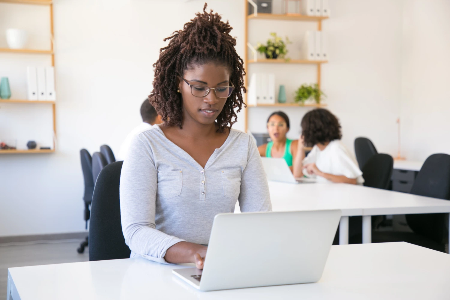 Mulher digitando em laptop em ambiente de coworking, mostrando o uso das noções de informática no dia a dia profissional e acadêmico.