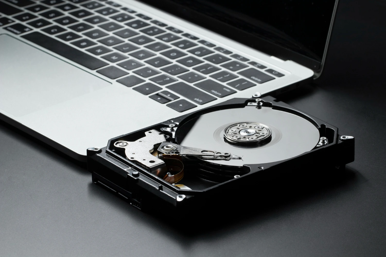 Disco rígido aberto ao lado de um notebook, simbolizando o conhecimento básico de hardware incluído nas noções de informática.
