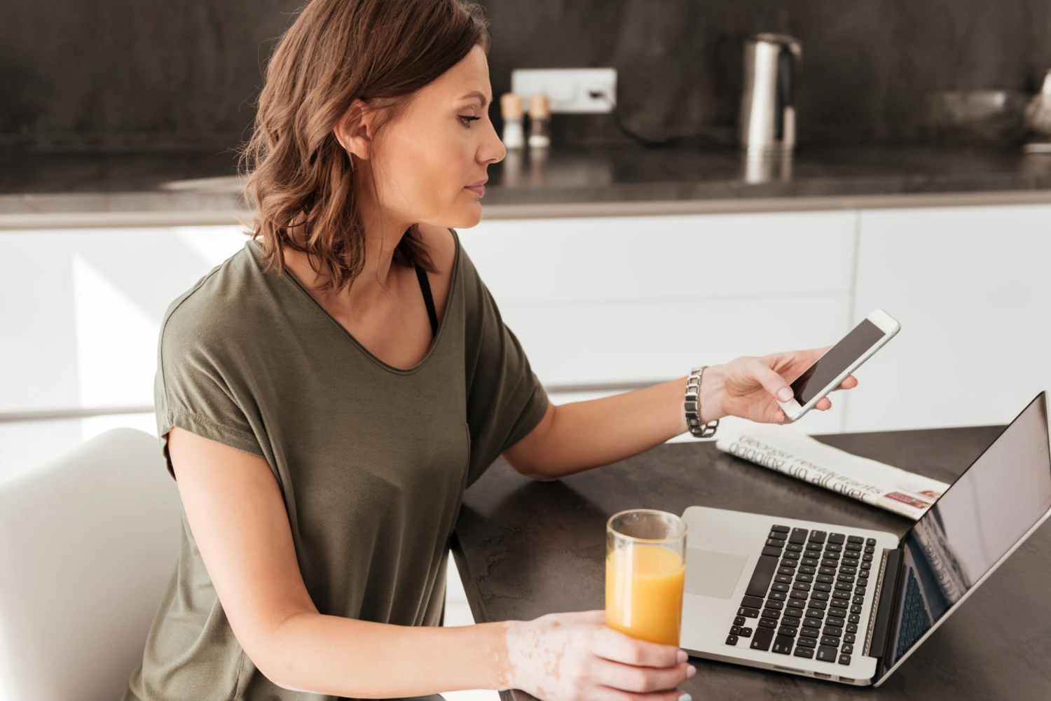 Mulher usando o celular e notebook simultaneamente, ilustrando o uso cotidiano das noções de informática para multitarefas e conectividade.