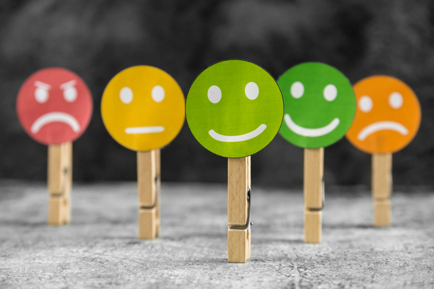 Uma sequência de ícones coloridos representando diferentes emoções, desde tristeza até felicidade. Cada ícone é fixado em um prendedor de roupa, simbolizando a variedade e o espectro das habilidades emocionais que precisamos reconhecer e gerenciar no dia a dia.