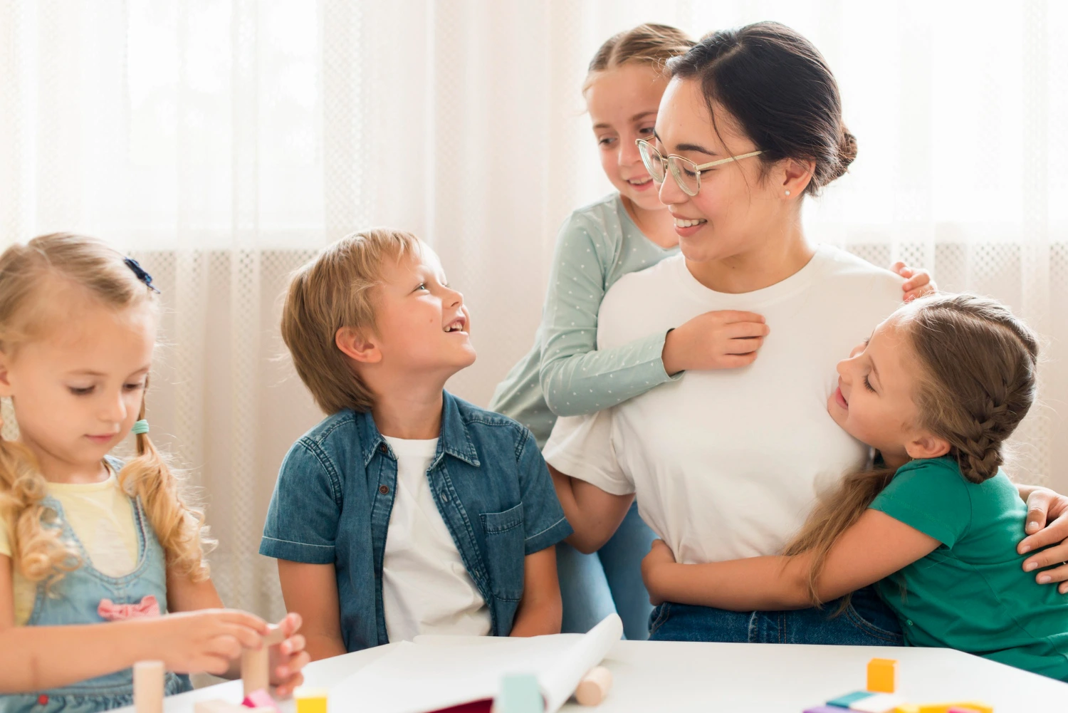 Uma educadora abraça crianças em uma sala clara e acolhedora. As expressões felizes indicam conexão e afeto. A imagem ressalta a relevância das habilidades emocionais na criação de ambientes seguros e positivos, nos quais as pessoas se sentem apoiadas e entendidas.