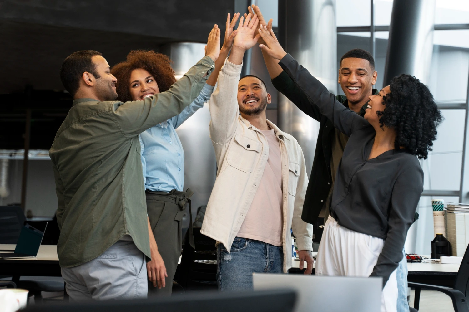 Equipe reunida dando high five com expressões felizes em ambiente corporativo – contraste com os riscos psicossociais no trabalho quando há ausência de apoio social.