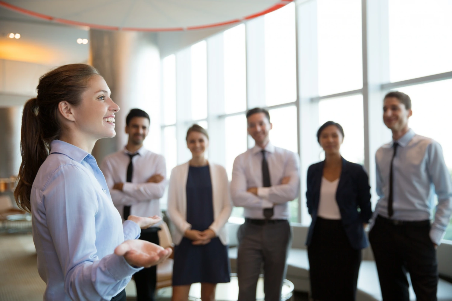 Imagem de uma mulher liderando uma equipe, demonstrando uma liderança de sucesso. Ela fala enquanto a equipe a observa atentamente.