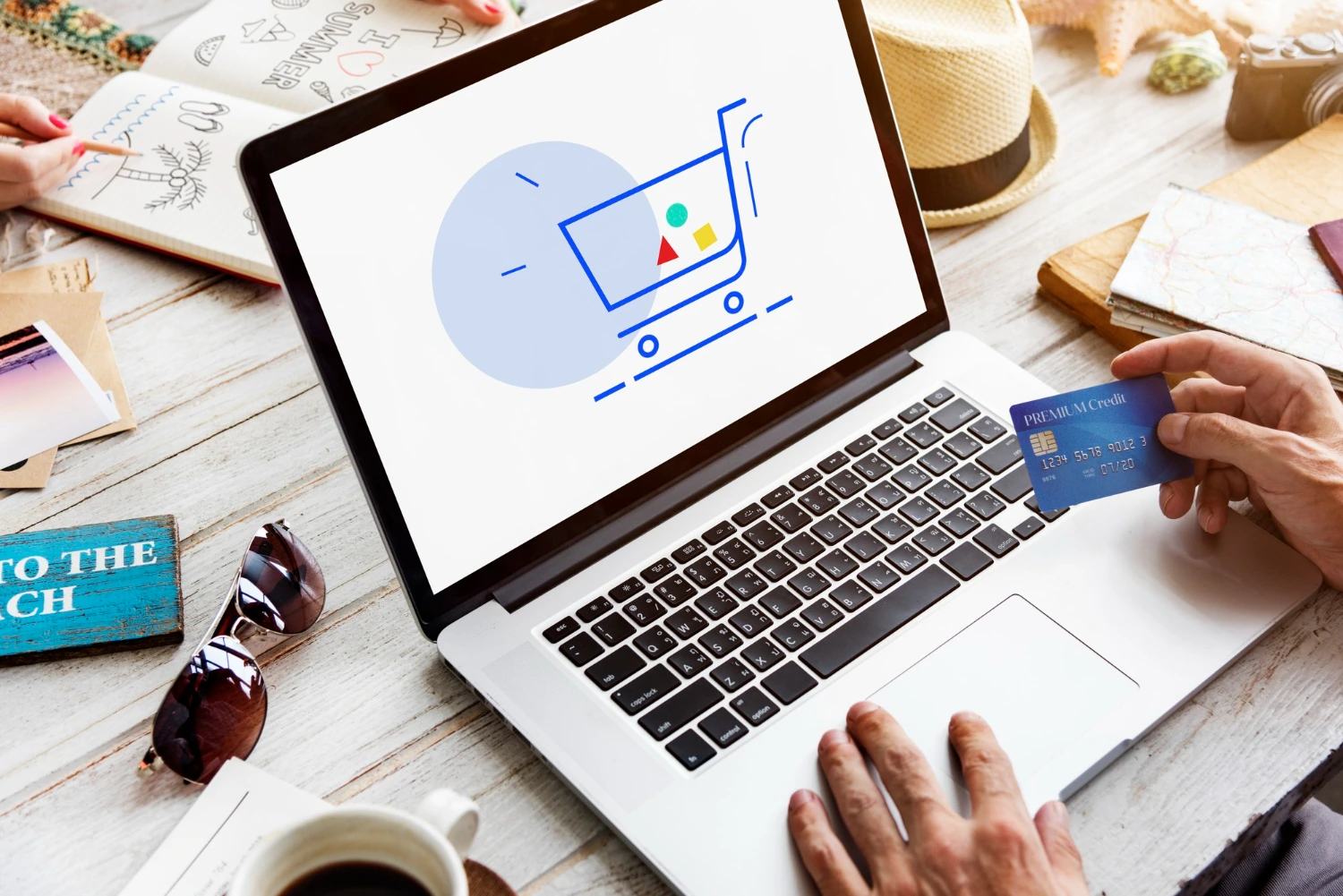 Pessoa segura cartão de crédito diante de notebook com ícone de carrinho de compras, representando o empreendedorismo digital no comércio eletrônico.