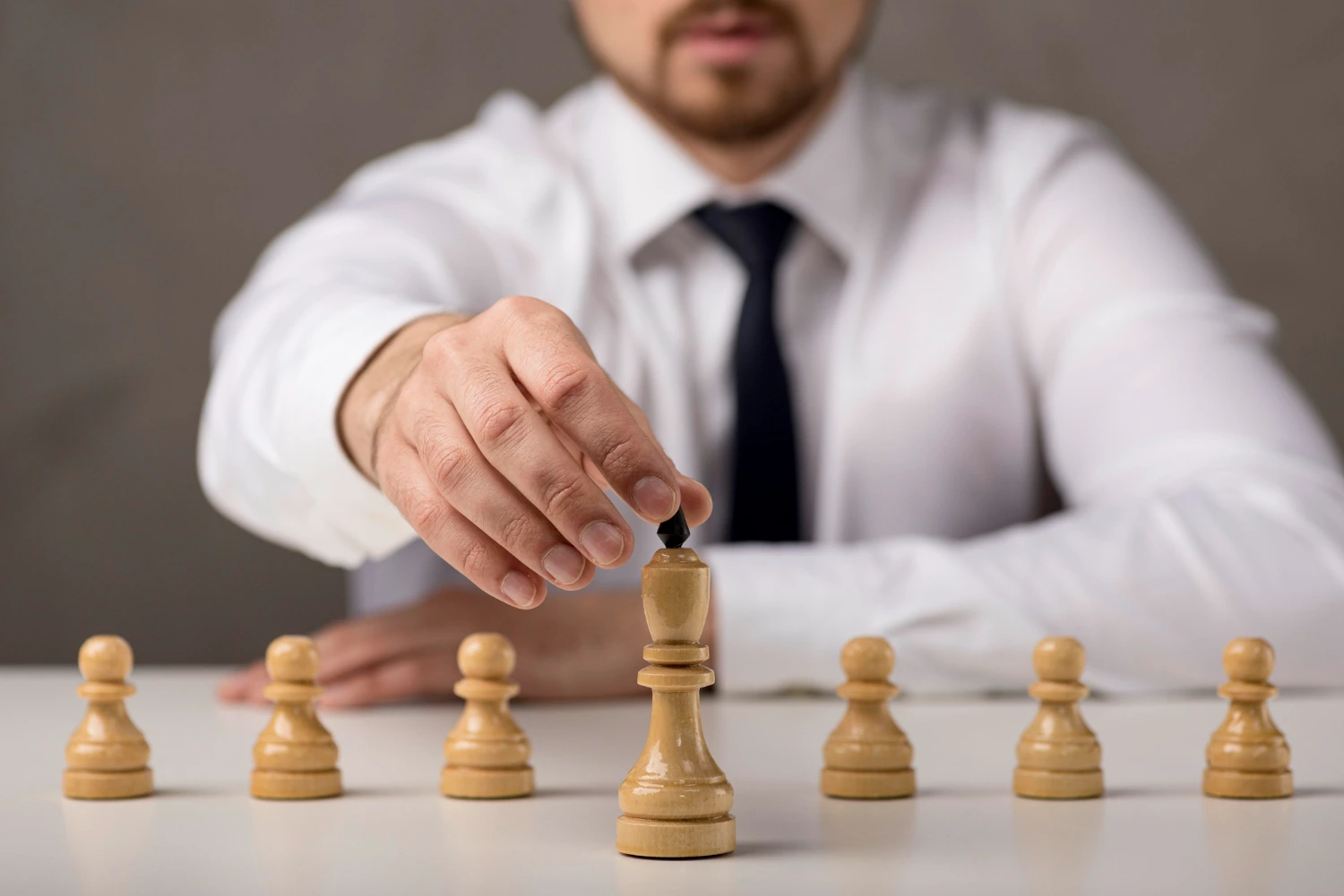 Homem move peça de xadrez em meio a peões, simbolizando tomada de decisão e diferentes tipos de liderança em contextos estratégicos.