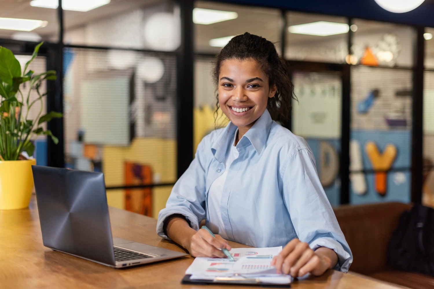 Mulher jovem e sorridente em um escritório moderno, com um laptop e documentos, refletindo sobre o que é carreira executiva.