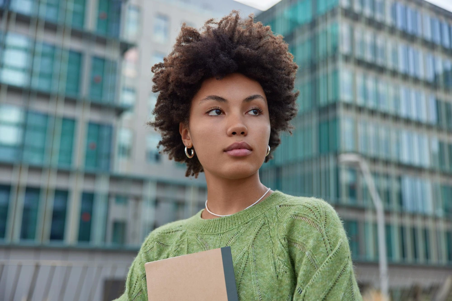 Mulher jovem com cabelos crespos, pensativa e confiante em frente a um prédio, refletindo sobre como escolher um concurso ideal.