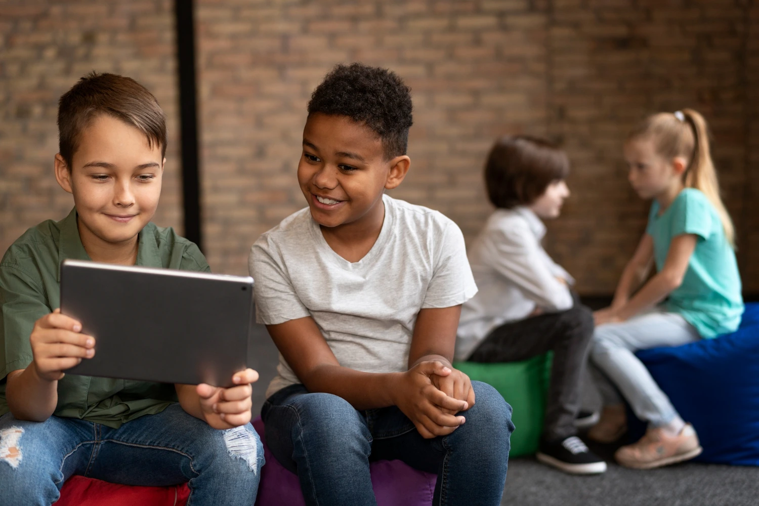 Dois meninos observam um tablet com entusiasmo enquanto outros colegas conversam ao fundo, simbolizando o futuro da educação com uso de recursos tecnológicos e interação social no aprendizado.
