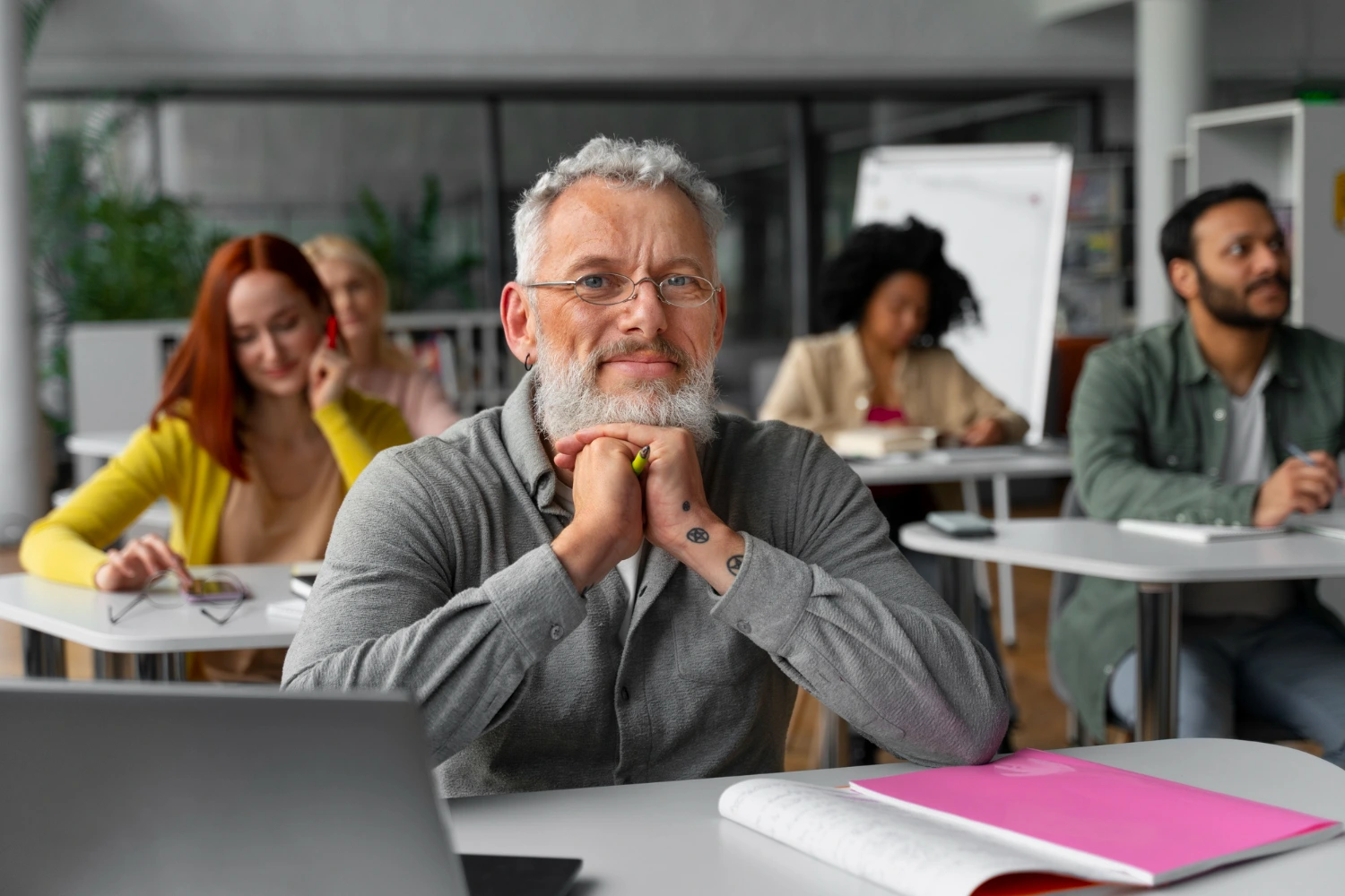 Homem de cabelos grisalhos e expressão confiante participa de um curso de atualização com outros educadores. A imagem ilustra o lifelong learning para professores como uma jornada de aprendizado permanente e troca de experiências.