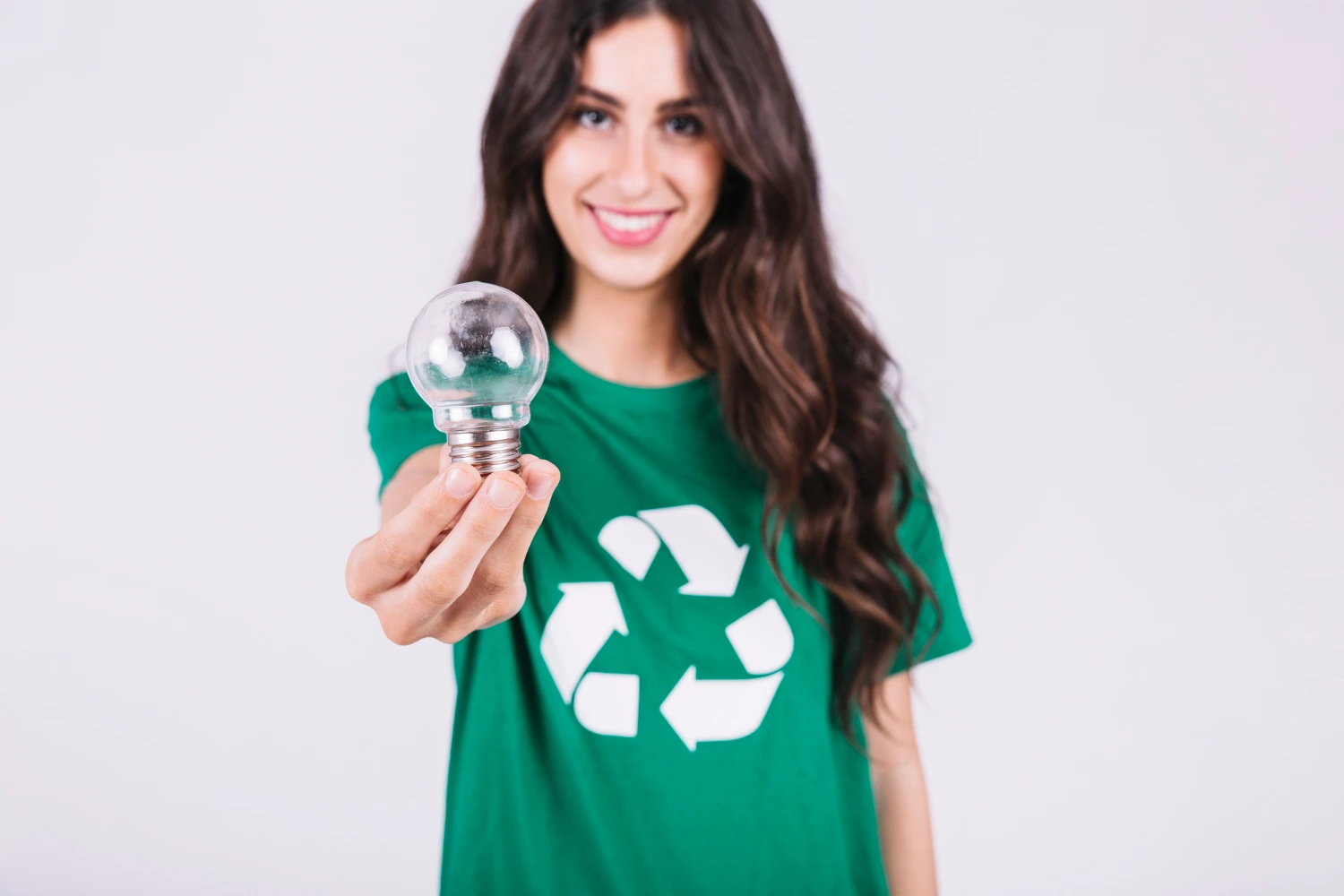 Mulher segurando uma lâmpada usada enquanto veste uma camiseta com símbolo de reciclagem, ilustrando práticas educativas sobre como descartar lixo eletrônico de forma correta e sustentável.