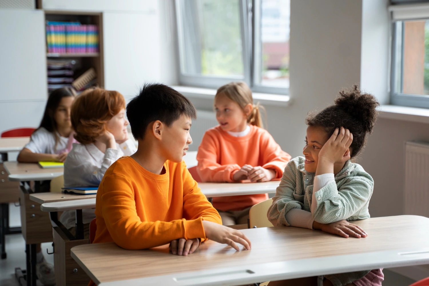 Crianças de diferentes etnias interagem em sala de aula, conversando e aprendendo juntas, ilustrando o papel da educação na inclusão social desde a infância.
